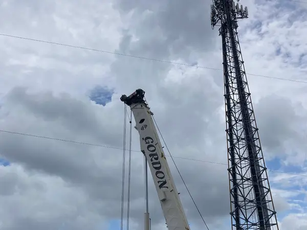 Gordon Crane's boom extended beside a lattice cell tower, the red and white crane and a shipping container in the foreground.