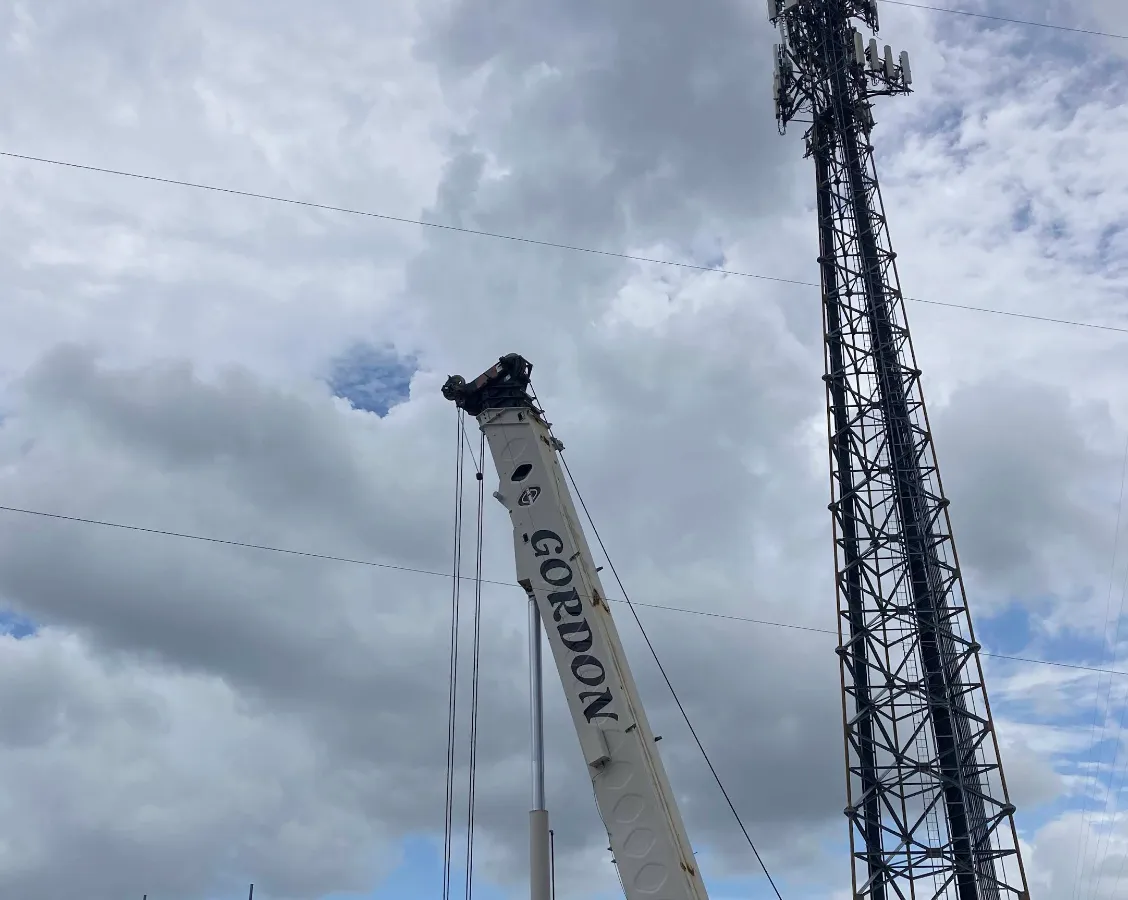 Gordon Crane's boom extended beside a lattice cell tower, the red and white crane and a shipping container in the foreground.