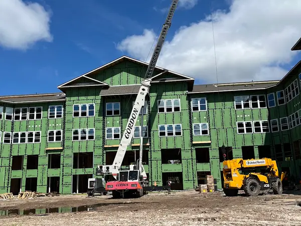 Gordon Crane's boom raised over the roofline of a three-storey timber-framed apartment building still in green sheathing, a telehandler working on the dirt below.