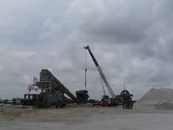 Gordon Crane's boom raised at an asphalt plant under heavy grey cloud, with the conveyor and stockpiles across the yard.