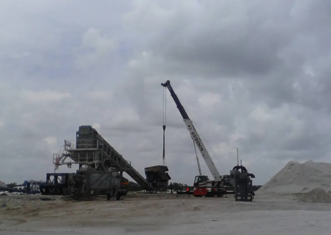 Gordon Crane's boom raised at an asphalt plant under heavy grey cloud, with the conveyor and stockpiles across the yard.