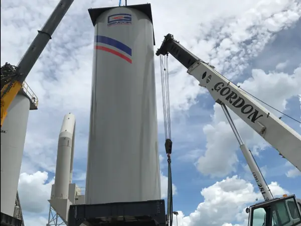 Two cranes setting a white GENCOR silo onto its steel base at a plant, Gordon Crane's boom and cab on the right.